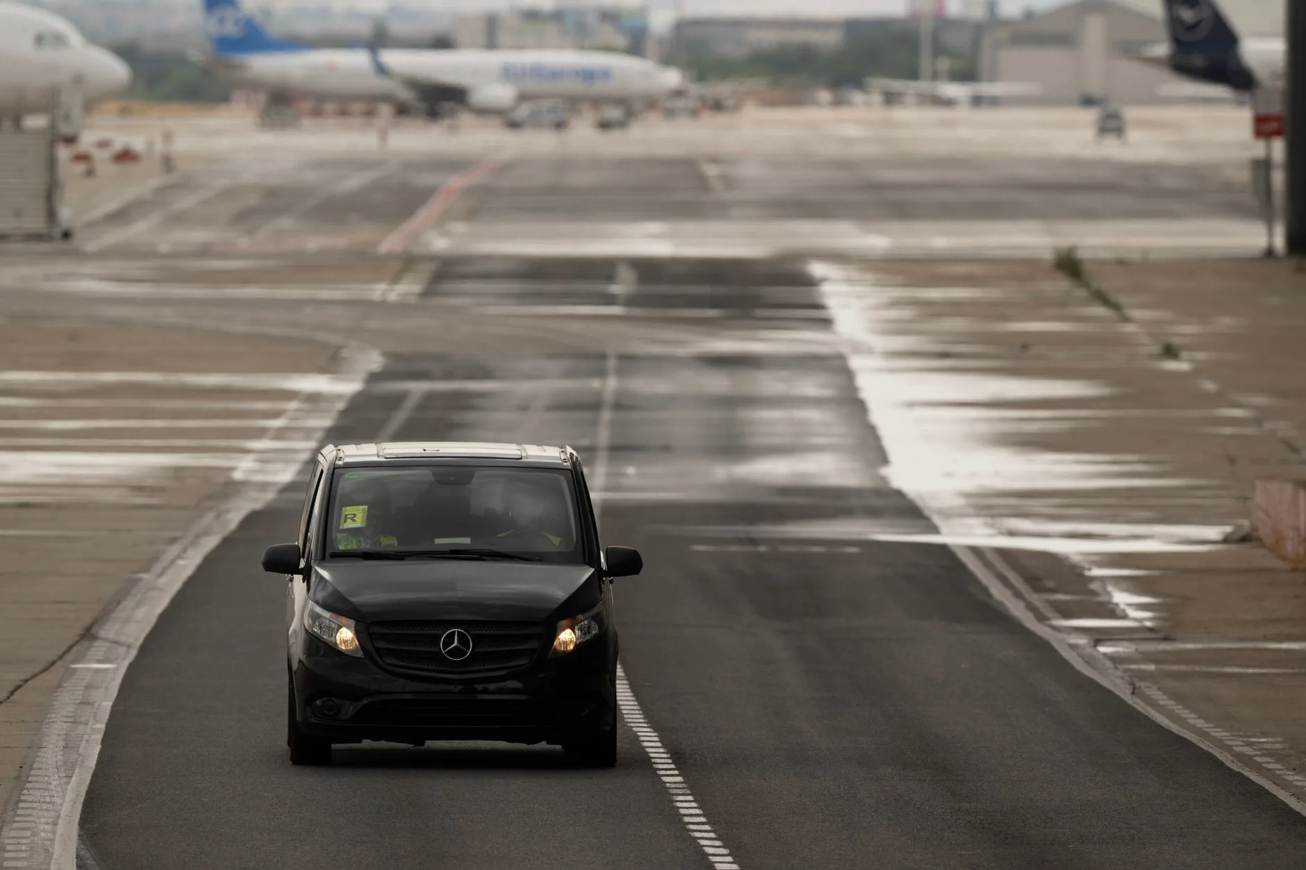 Luxury car driving across an airport tarmac towards the terminal.